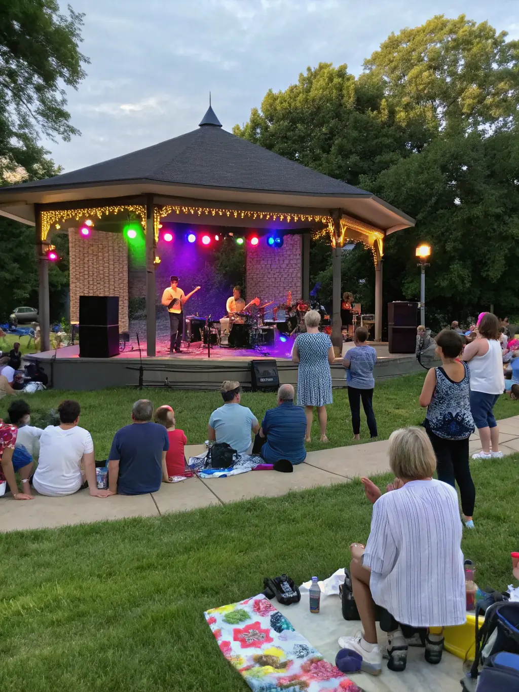 A vibrant image of a DYNAMIC EVENTS-sponsored concert in a local park, featuring a local band performing for an enthusiastic audience.